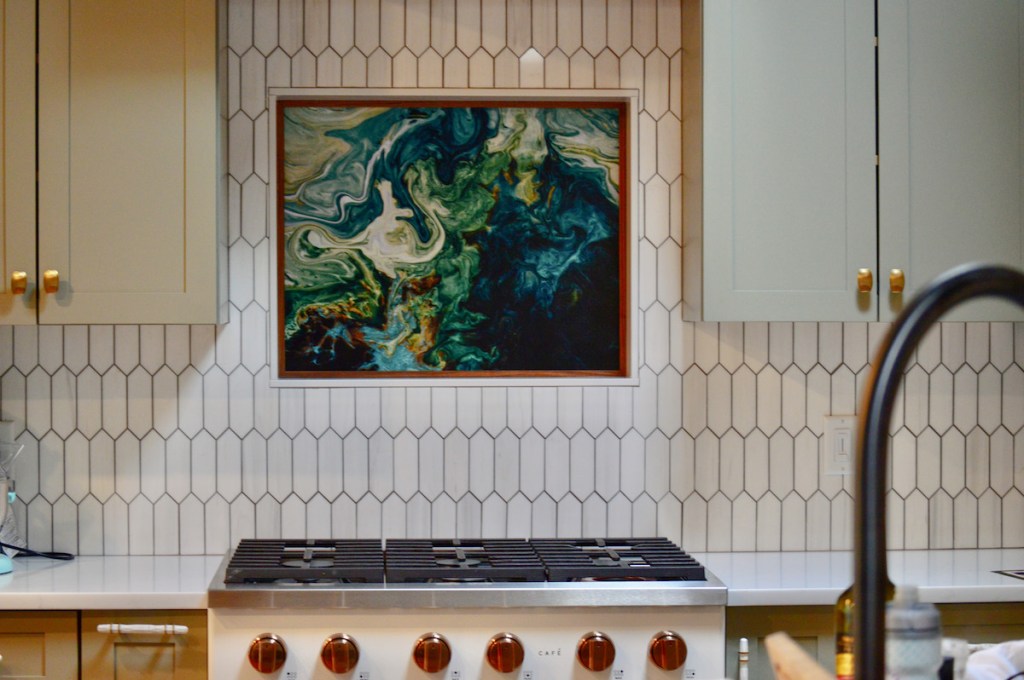 Original custom aluminum artwork, an abstract poured art painting in shade of green and blue, shown hanging above stovetop in an off-white kitchen